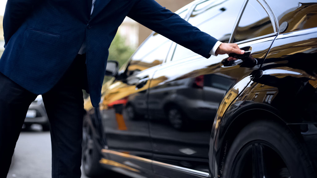 Chauffeur professionnel en costume sombre ouvrant la portière arrière d'une berline premium pour un client d'affaires
